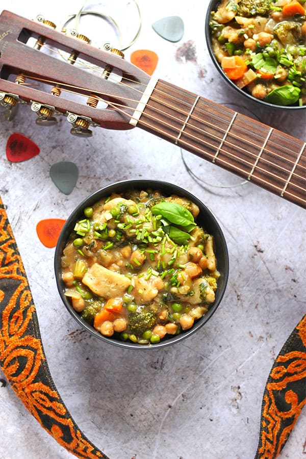 bowl of chickpea and vegetable dumpling stew with broccoli, carrots, kale and peas with guitar and strap.