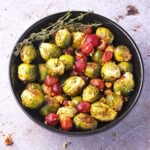 Baked Brussels sprouts with grapes, with thyme, walnuts and Balsamic vinegar in black bowl.