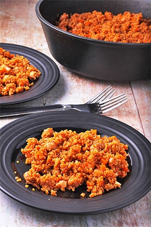 quinoa chickpea pilaf on black plates with fork and cast iron pot.
