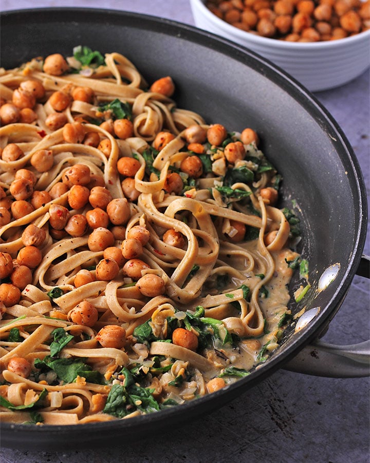 Chickpea pasta sauce with rosemary and spinach with tagliatelle in black skillet with chickpeas in background.