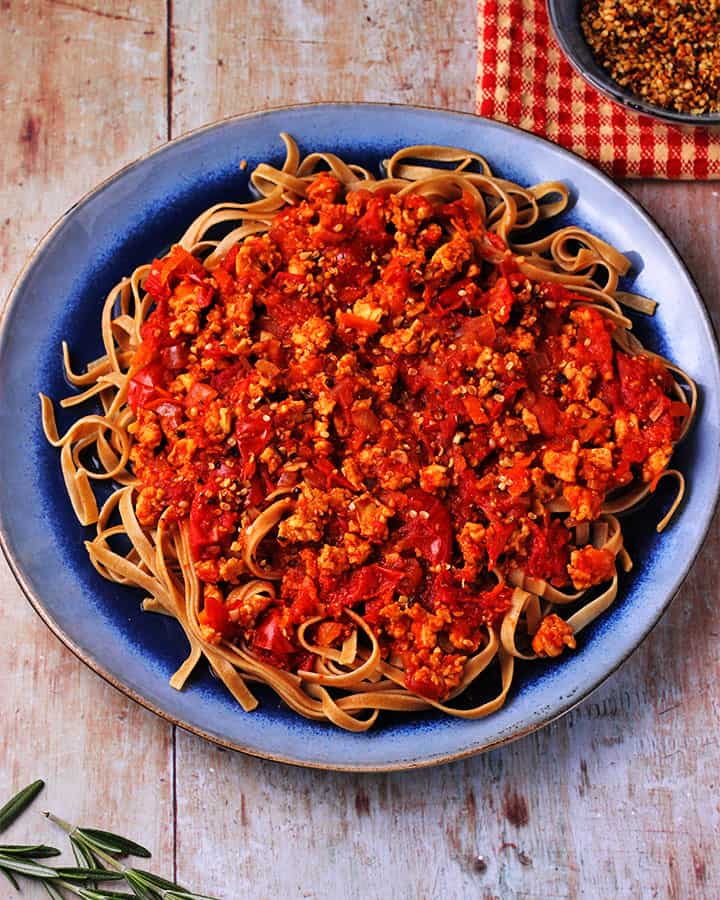 Tempeh Bolognese with wheat tagliatelli pasta on blue plate.