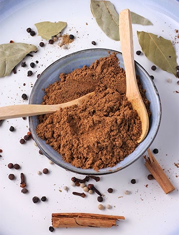 Baharat spice blend in small blue dish with small wooden spoons