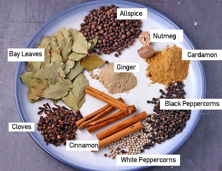 Baharat spices cloves, cinnamon, black and white peppercorns, bay leaves, nutmeg, allspice, ginger and cardamom on blue plate before blending