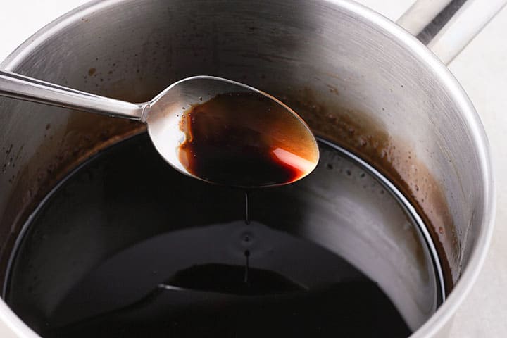 Balsamic vinegar is reduced in pan with spoon testing it.