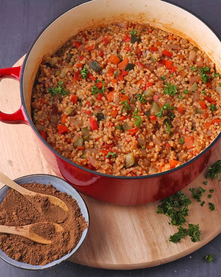 Red cooking pot of cooked bulgur with vegetables with chopped parsley and small bowl of Baharat.