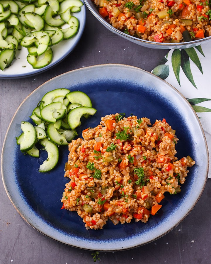 Cooked bulgur with vegetables on blue plate with cucumber-mint salad