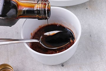 reduced balsamic vinegar is poured from bottle onto a spoon in a small white bowl.