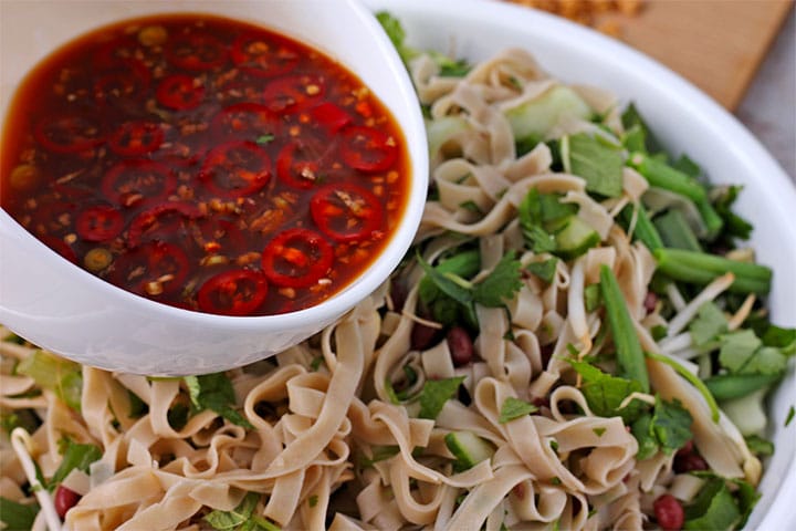 Dressing with sliced red chilies, lime juice, rice vinegar, minced garlic and soy sauce is poured over rice noodles, herbs and vegetables