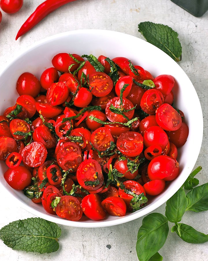 Thai tomato salad with sliced cherry tomatoes with sliced red chili, chopped basil and mint in white bowl