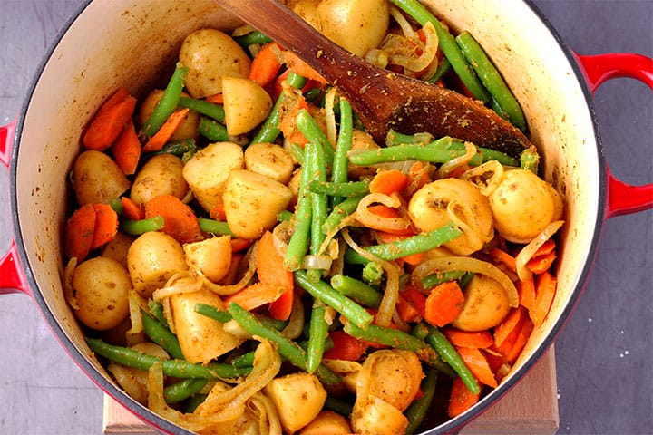 potatoes, carrots, green beans and onions with massaman curry paste in pan.