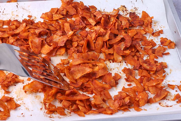 Brown coconut bacon flakes on baking sheet with parchment paper and silver spatula