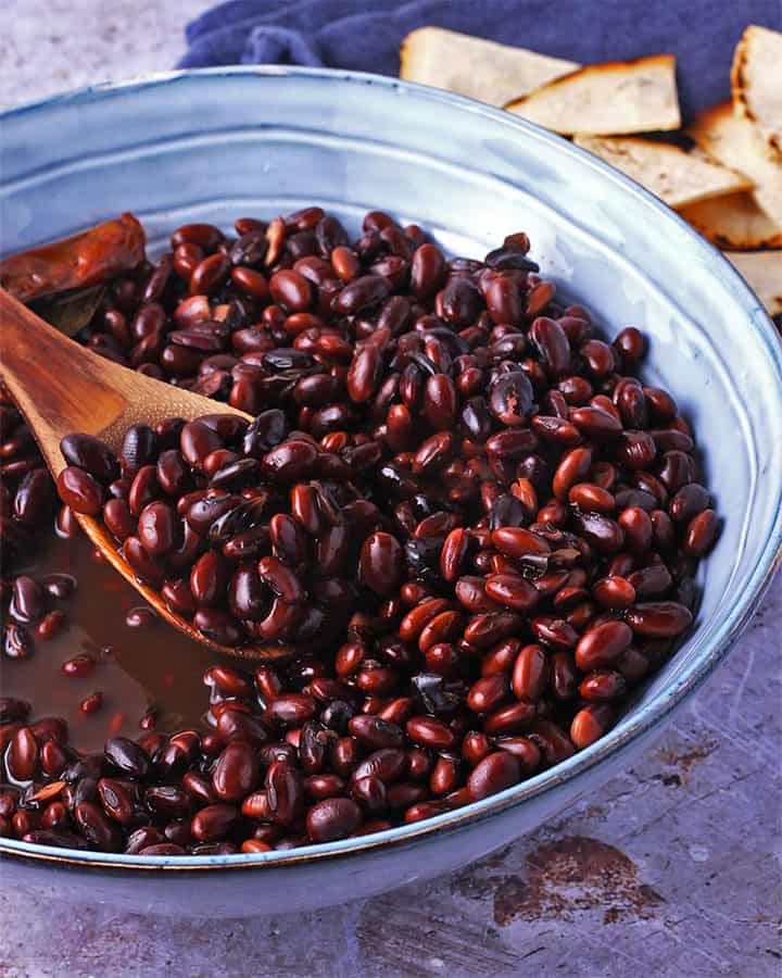 Cooked black beans in a blue bowl are stirred with a wooden spoon