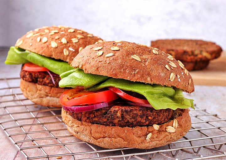 Deluxe tempeh burgers with buns, lettuce, red onion slices and tomatoes on wire rack