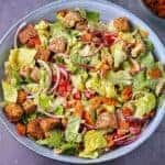 vegan Caesar salad in blue bowl with coconut bacon, croutons, lettuce, cherry tomatoes and red onions in blue bowl.