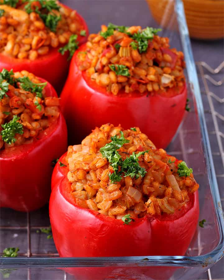 Whole red pepper stuffed with barley and white beans and tomato sauce in glass baking dish