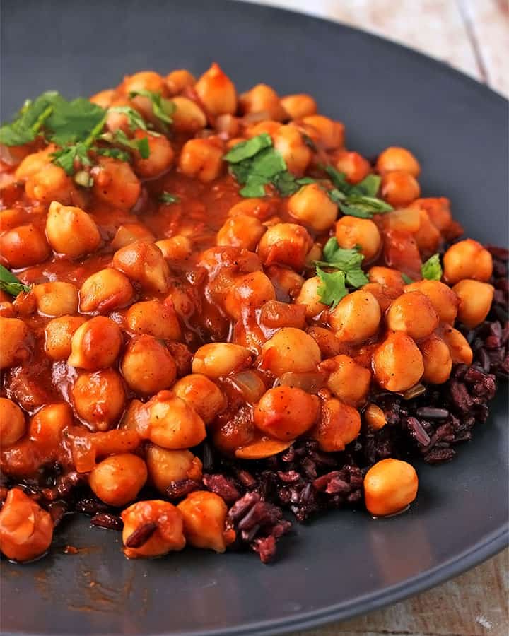 chickpea curry masala with tomato sauce on black plate with black rice and chopped cilantro
