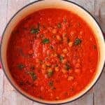 cooking pot with chickpeas in red pepper sauce with chopped parsley garnish