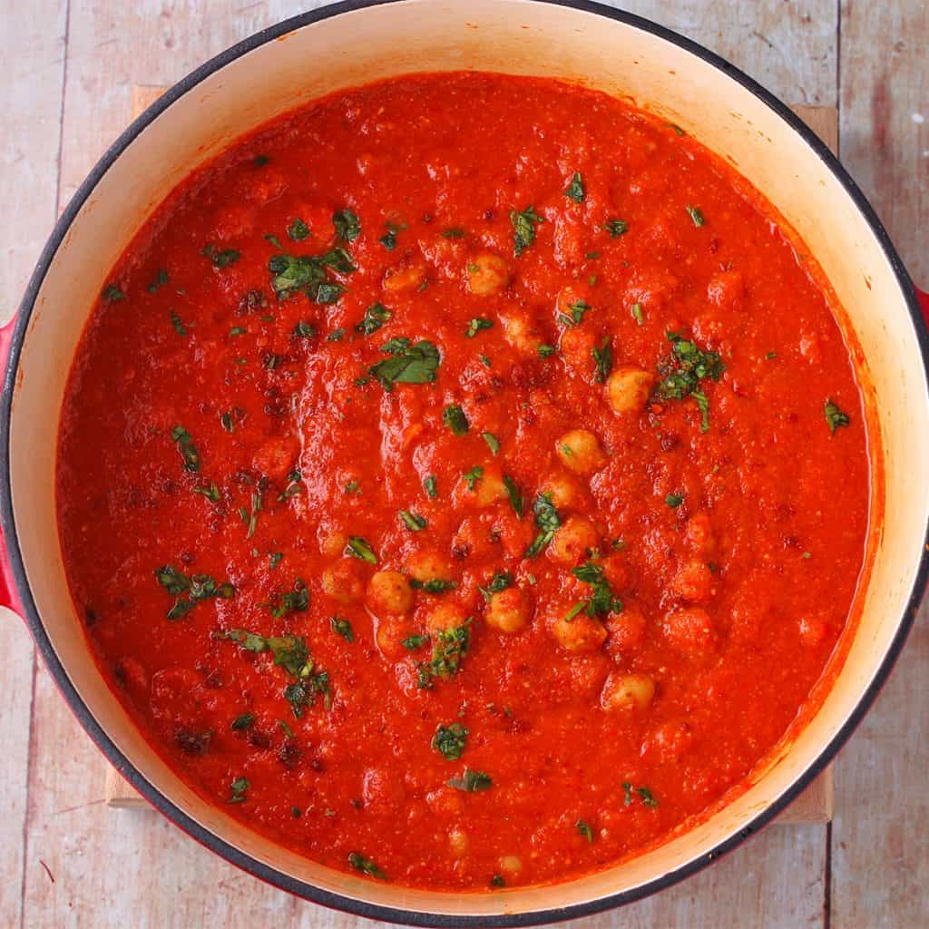 cooking pot with chickpeas in red pepper sauce with chopped parsley garnish