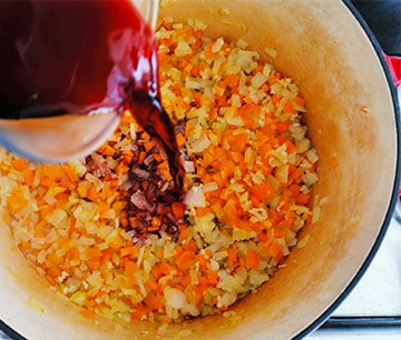 Red wine is poured into pot with diced carrots and onions.
