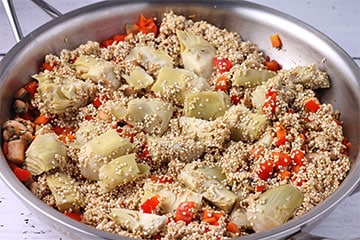 sliced artichoke hearts and dried quinoa is added to steel pan with red peppers.