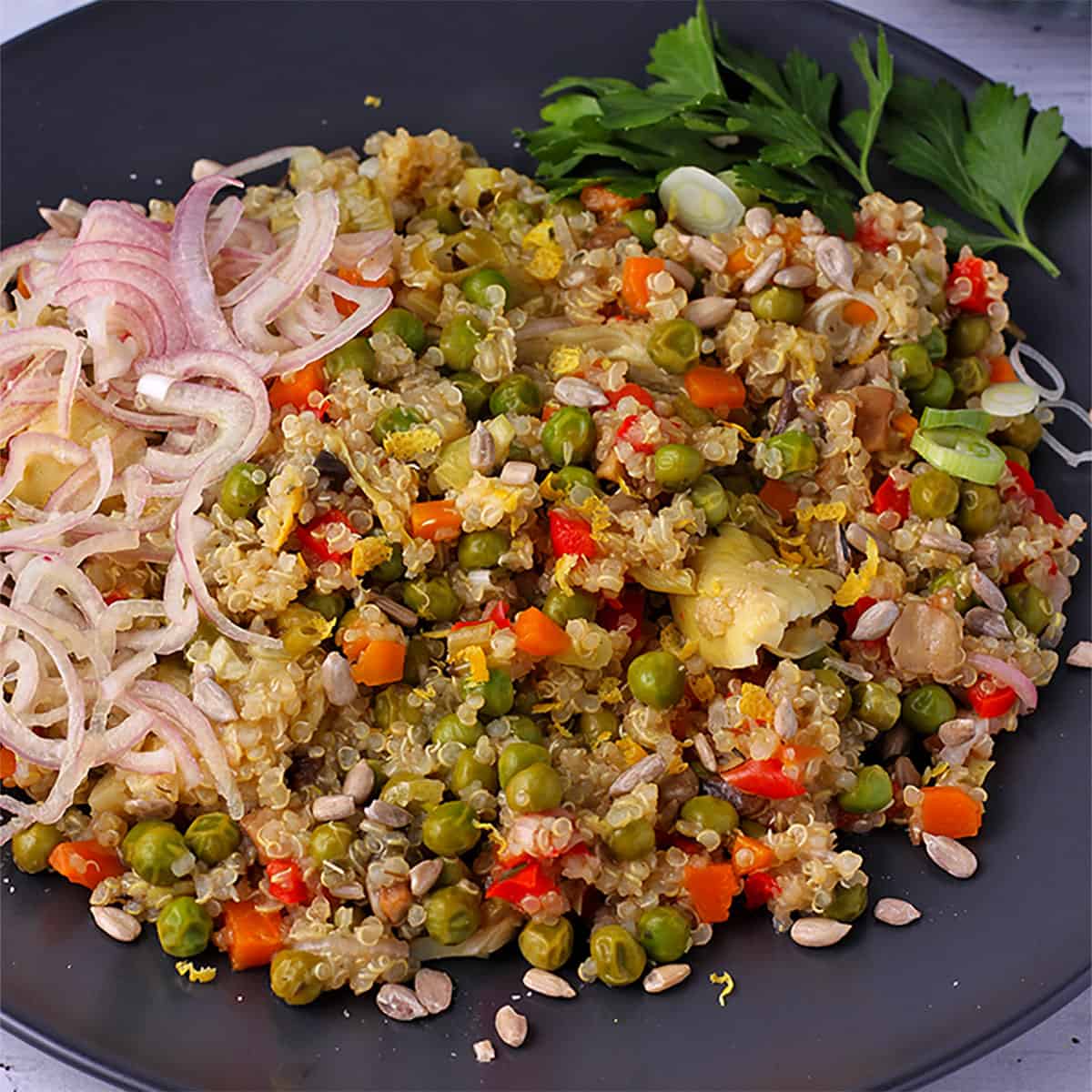 Cooked quinoa with vegetables on black plate with sliced shallots.