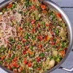 cooked quinoa with vegetables, sunflower seeds and sliced shallots in steel pan.