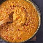 Sweet potato dahl with red lentils overhead in black pot with wooden spoon and red chili flakes on top