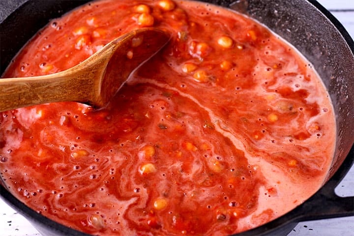 Pureed tomatoes and coconut milk is added to black pan with chickpeas