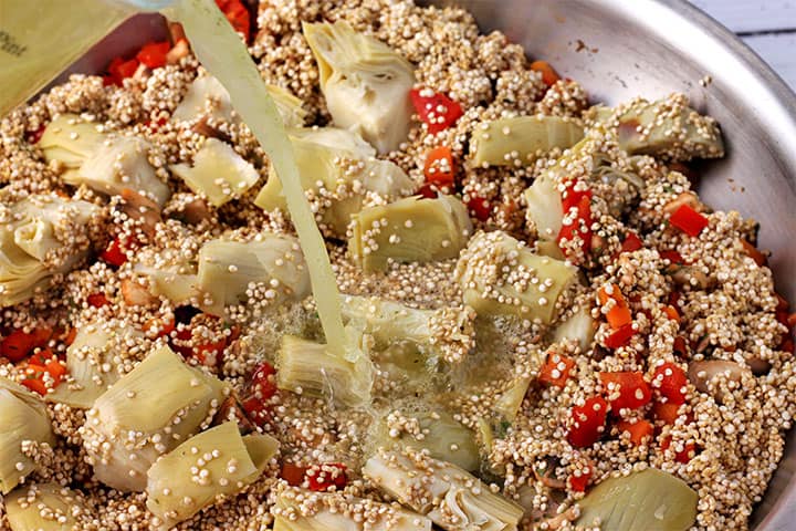 Vegetable broth is poured over quinoa, artichoke hearts, mushrooms, red peppers, and carrots