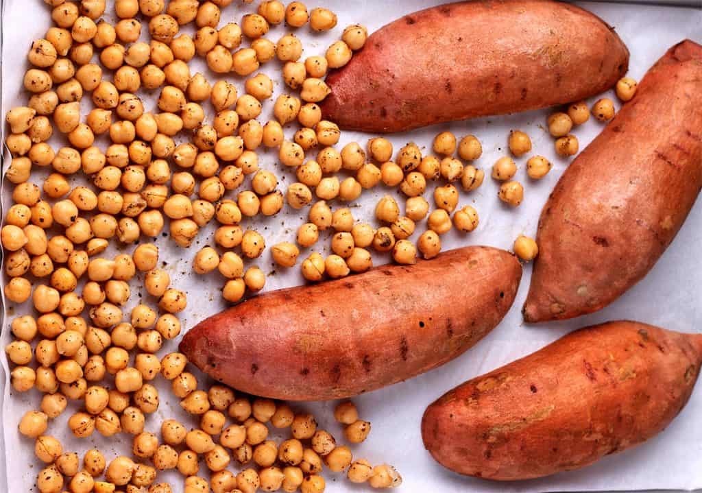 4 sweet potato halves on baking tray (skin-side up) with chickpeas.
