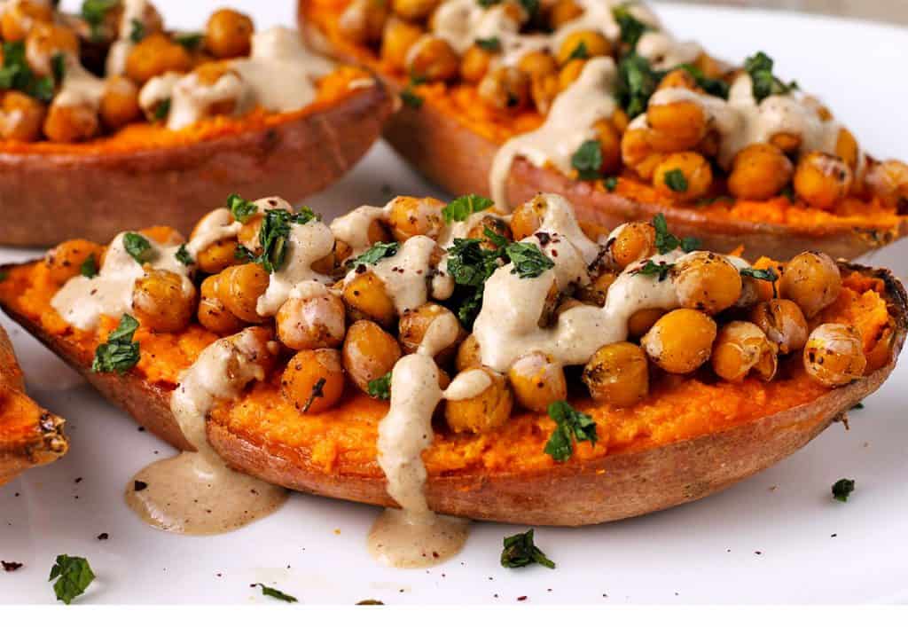 side view of a baked sweet potato with baked chickpeas, dressing and chopped mint