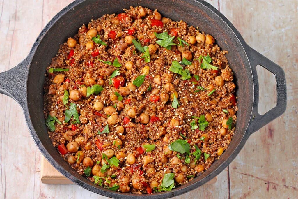 Chickpeas and quinoa with red pepper and chopped parsley in black cooking pot.