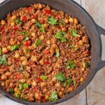 chickpeas and quinoa cooked in black cast iron pot with chopped parsley and red peppers