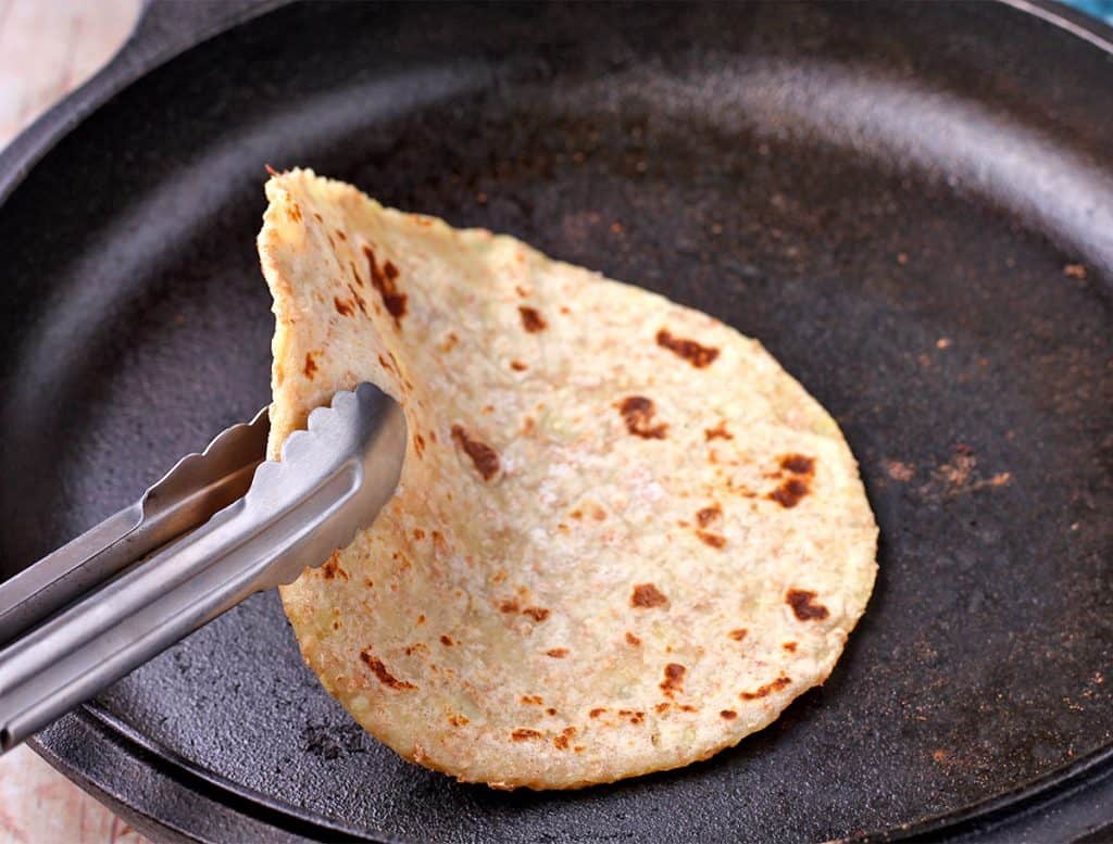 flatbread in cast iron pan being flipped with tongs