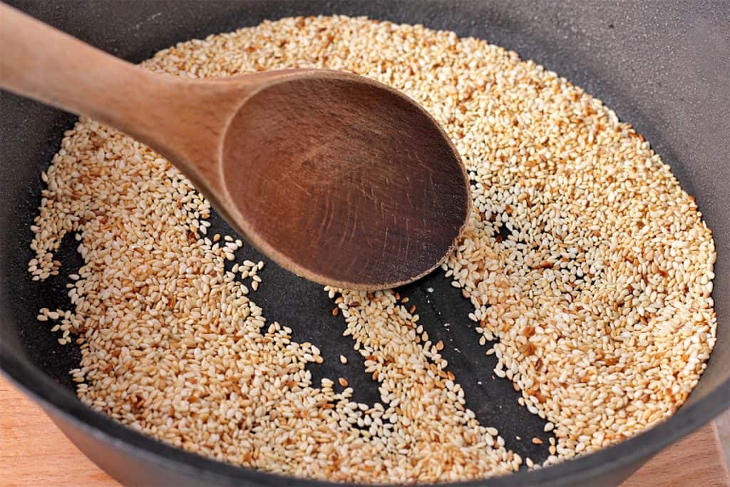 sesame seeds are toasted in black pan and stirred with a wooden spoon
