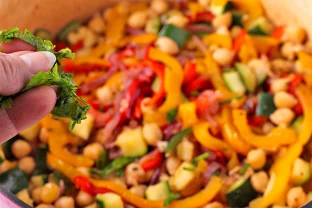 chopped parsley is added to pot with sliced red and yellow bell peppers, diced zucchini, red onions and chickpeas.