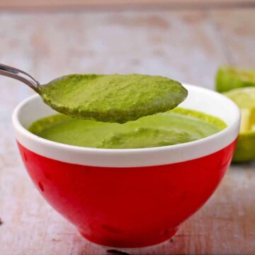 A spoonful of cilantro lime dressing is held over red bowl