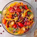 tomato and pomegranate salad in glass bowl with sliced yellow pepper and red onion and fresh basil and mint and bowl of Za'atar spice blemd
