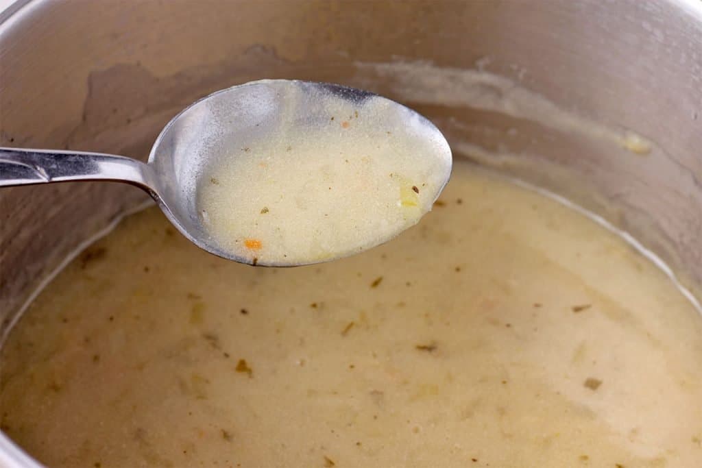 Spoonful of tarragon sauce is held over a saucepan of sauce