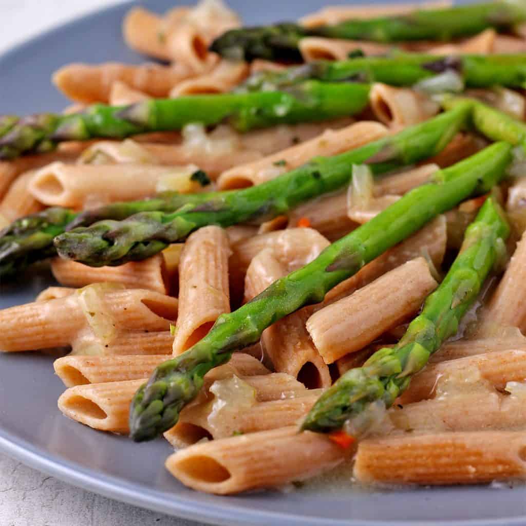 Asparagus tips and whole wheat pasta with tarragon sauce on blue plate