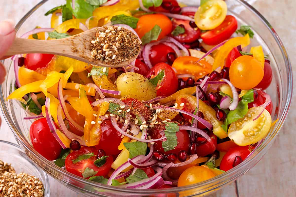 zaatar spice blend with sesame seeds is added to tomato and pomegranate salad