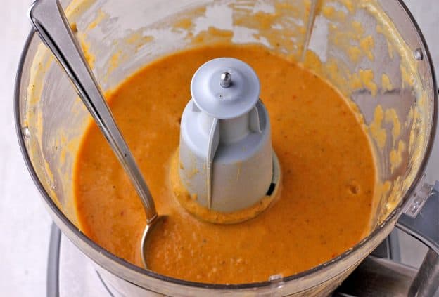 Sauce with blended chickpeas and carrots in food processor with spoon