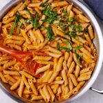 chickpea sauce with cooked penne pasta in skillet with a wooden spoon