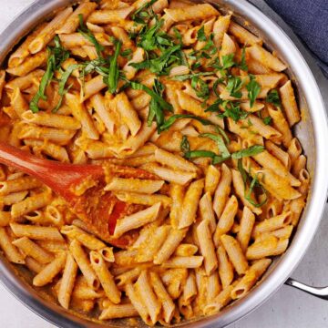 chickpea sauce and cooked penne pasta with wooden spoon in a silver skillet