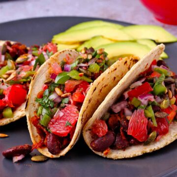 3 tacos with kidney beans, grapefruit salsa, and pepitas on black plate