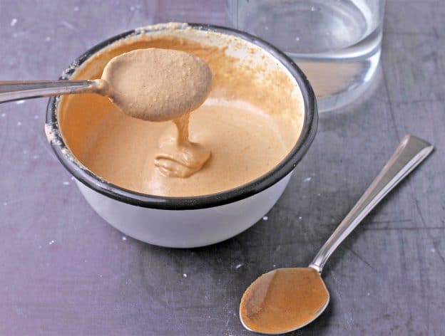 tahini is dripping from a spoon into a bowl