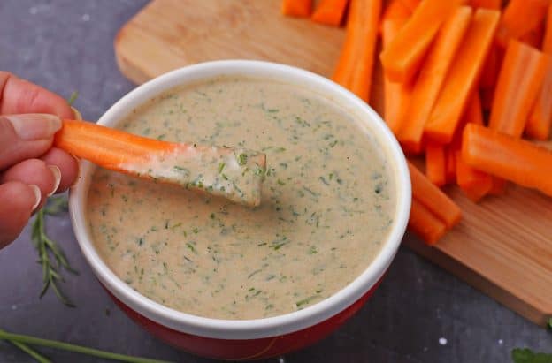 a carrot stick is dipped into tahini ranch dressing
