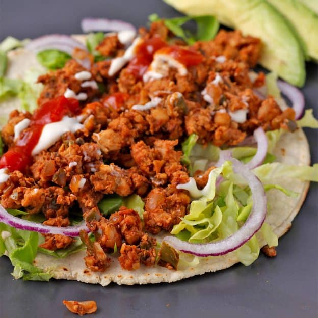 Taco with tempeh taco meat, sliced red onion, lettuce, salsa, and cashew sour cream