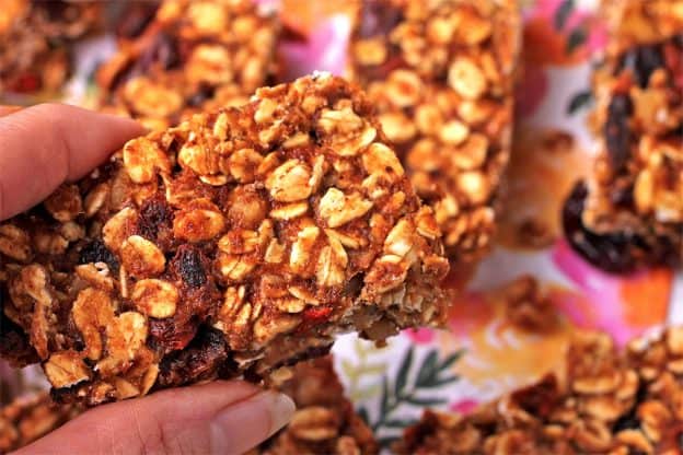 Baked sugar-free granola bar with oats, dried cranberries, Goji beans, and walnuts held in hand.
