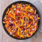 vegan coleslaw with mango, red and green cabbage, carrots, and chopped cilantro in black bowl.